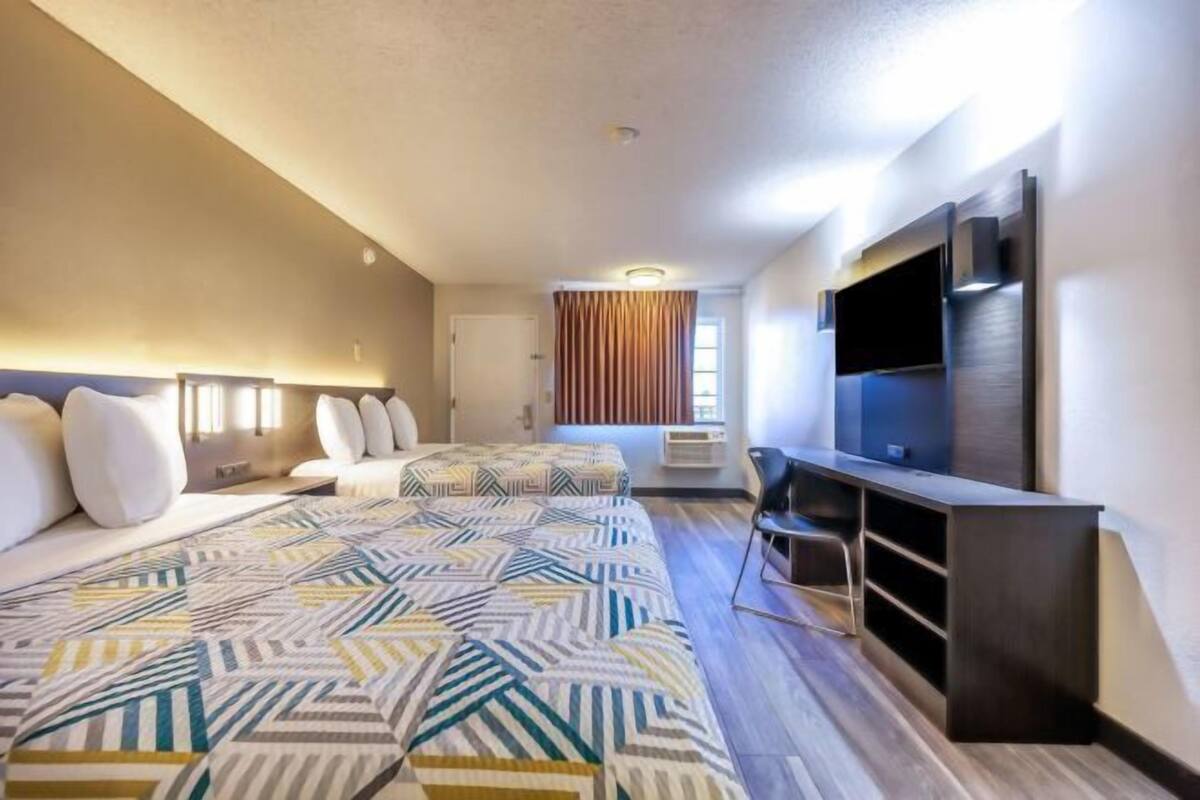 Une chambre d’hôtel avec deux lits, une télévision, un bureau et une fenêtre avec des rideaux.