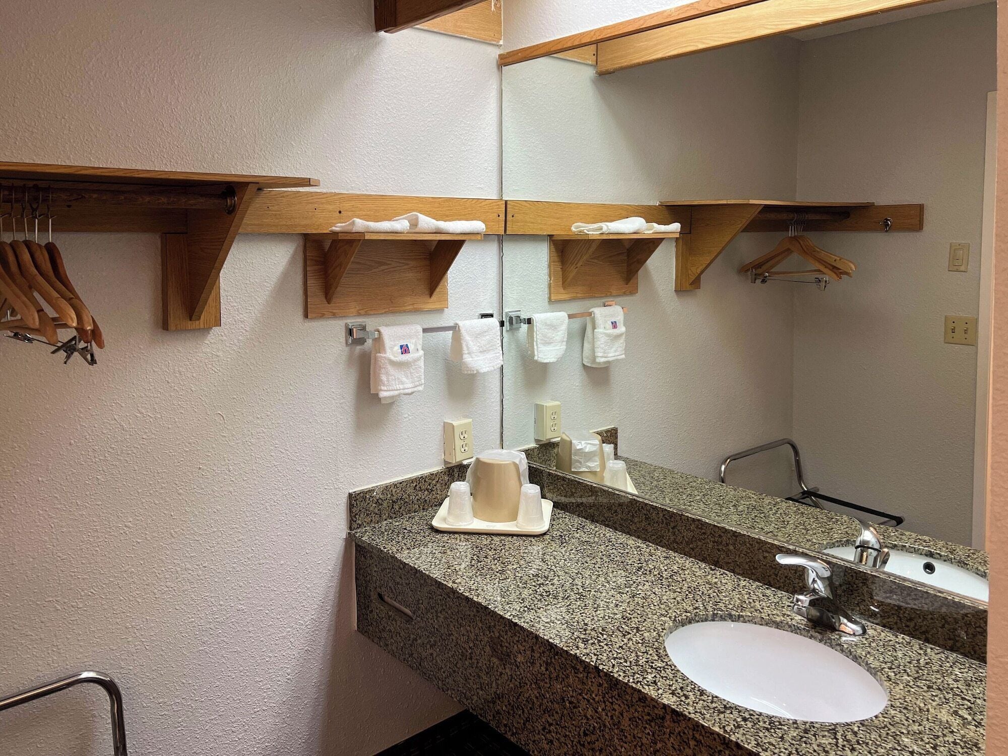 Un baño con encimera de granito, un lavabo blanco, un espejo y toalleros de madera.