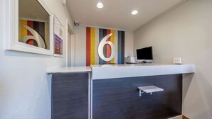 A reception desk with a large number '6' on the wall, a flat-screen TV, and a small shelf. - Motel 6 Portland, OR - Southeast (Portland)