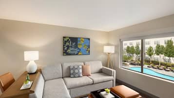 A hotel room with a grey sofa, a dining table with a lamp, a painting on the wall, and a view of a swimming pool outside.
