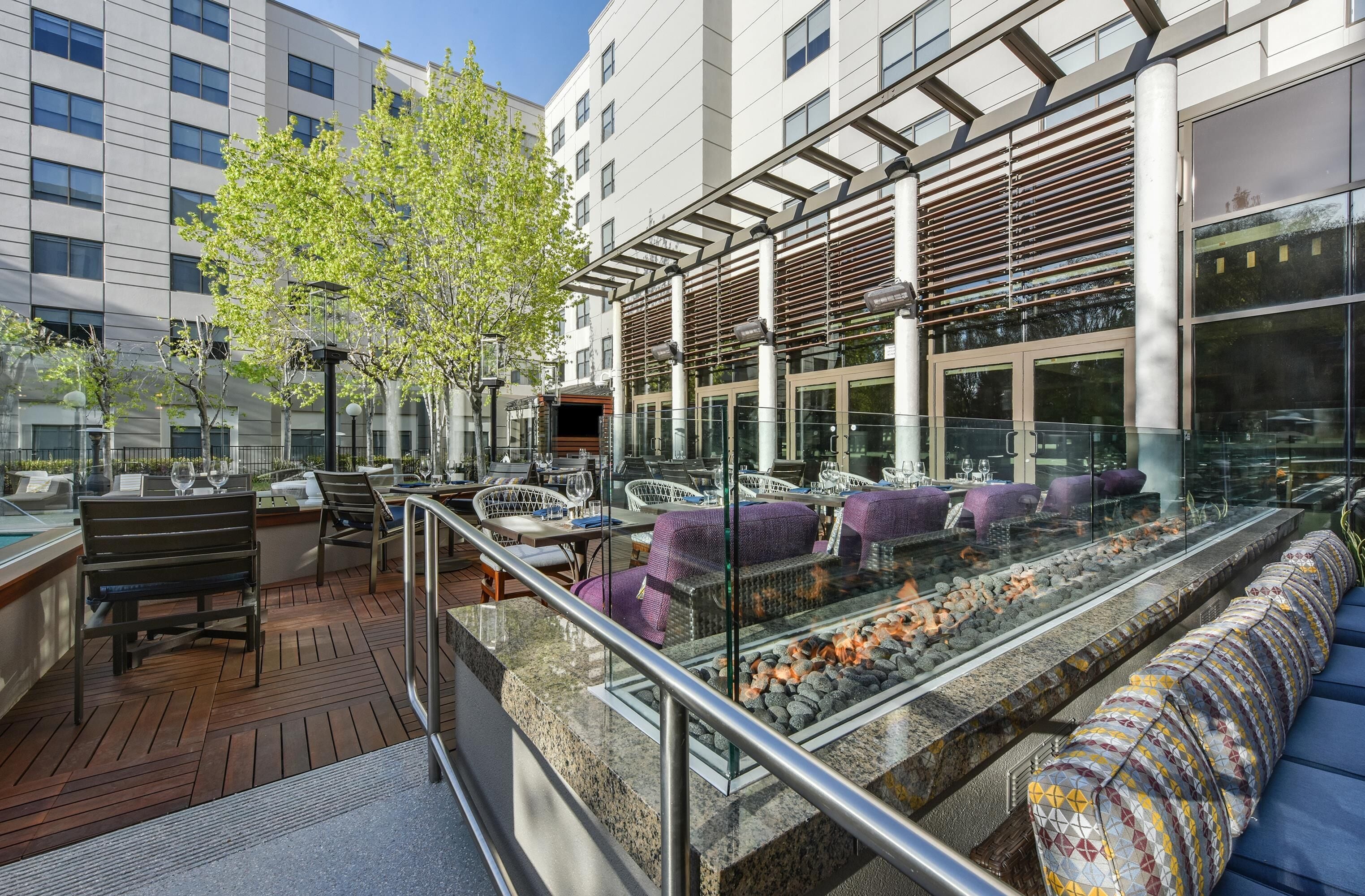 An outdoor seating area with tables and chairs, a fire feature, and a view of the building's facade.