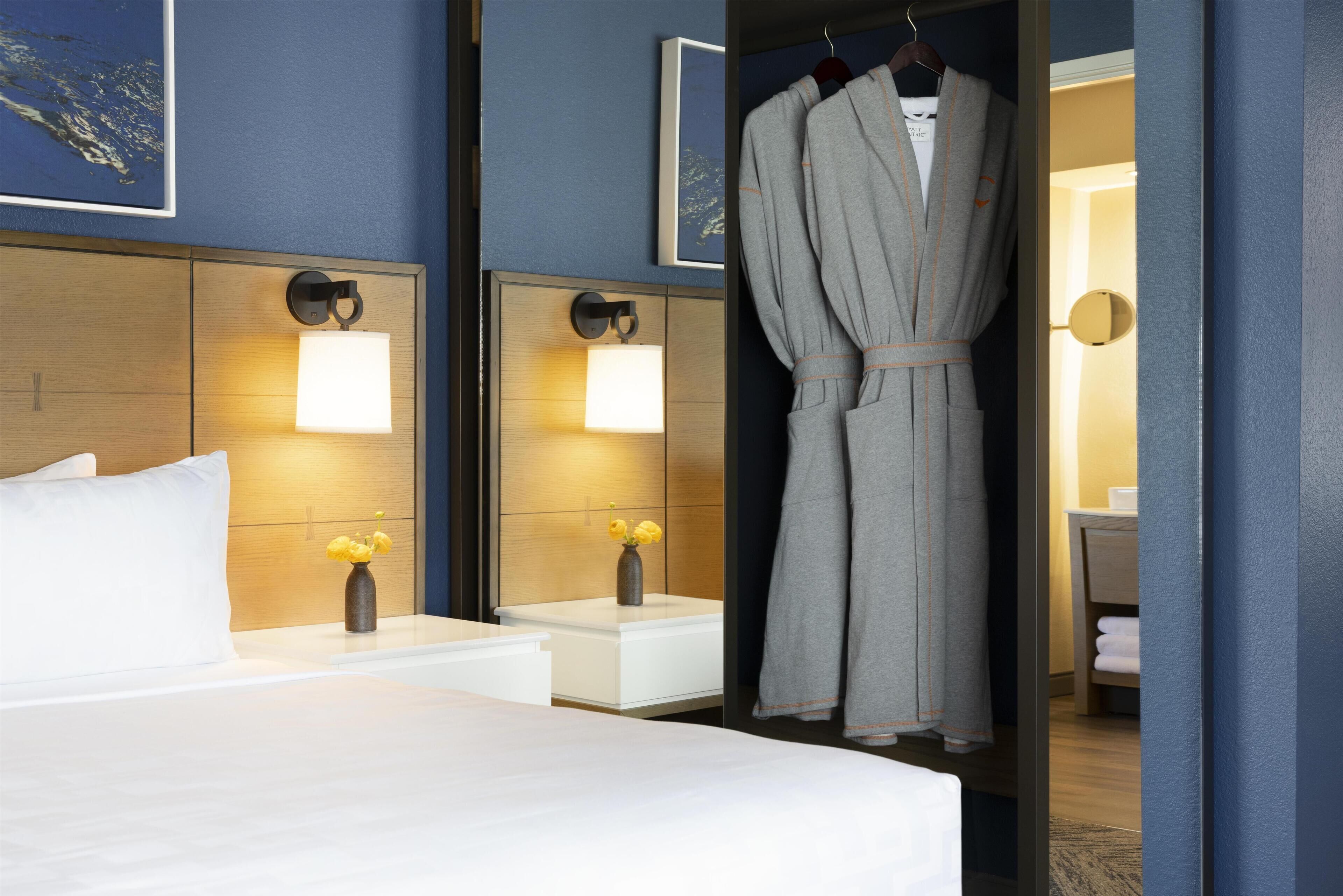 A hotel room with a bed, bedside tables, a robe hanging, and a mirror.
