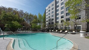 Una piscina con borde curvo, rodeada de sillas de descanso y un edificio con múltiples ventanas.