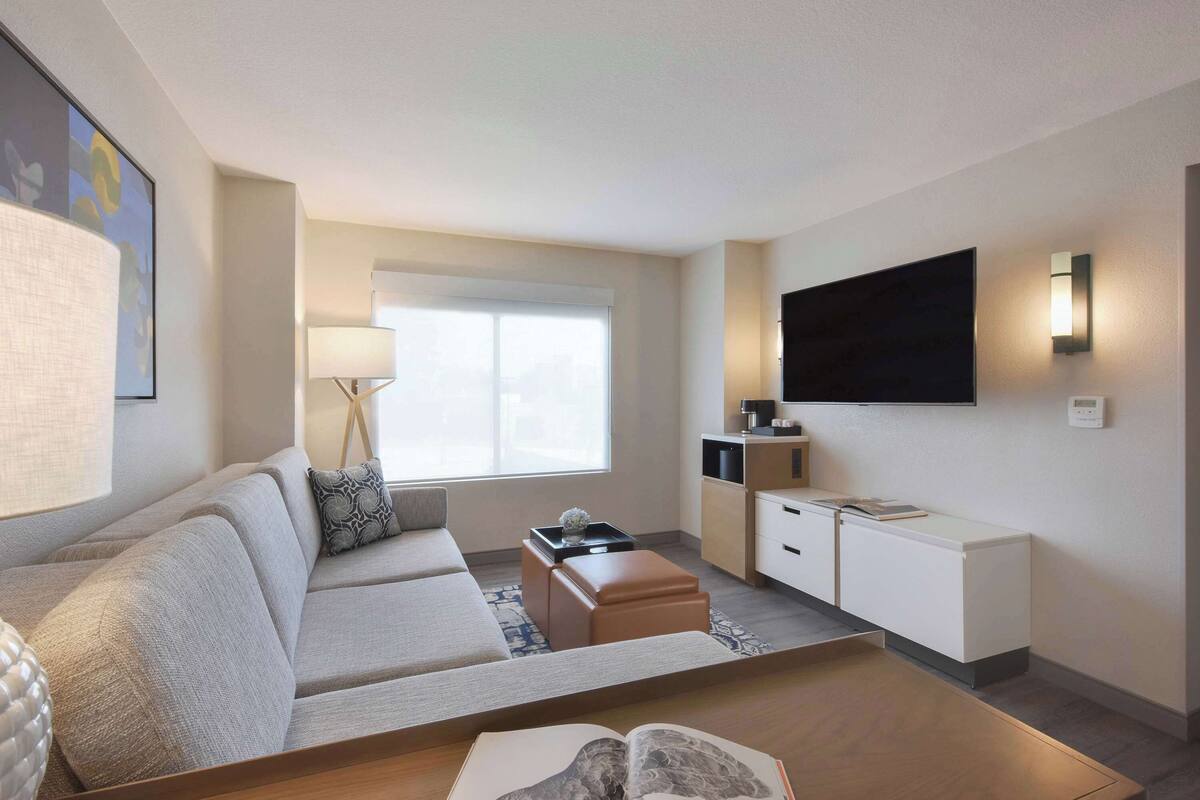 Une chambre d’hôtel moderne équipée d’un canapé, d’une table basse, d’une télévision et d’un bureau avec une lampe.