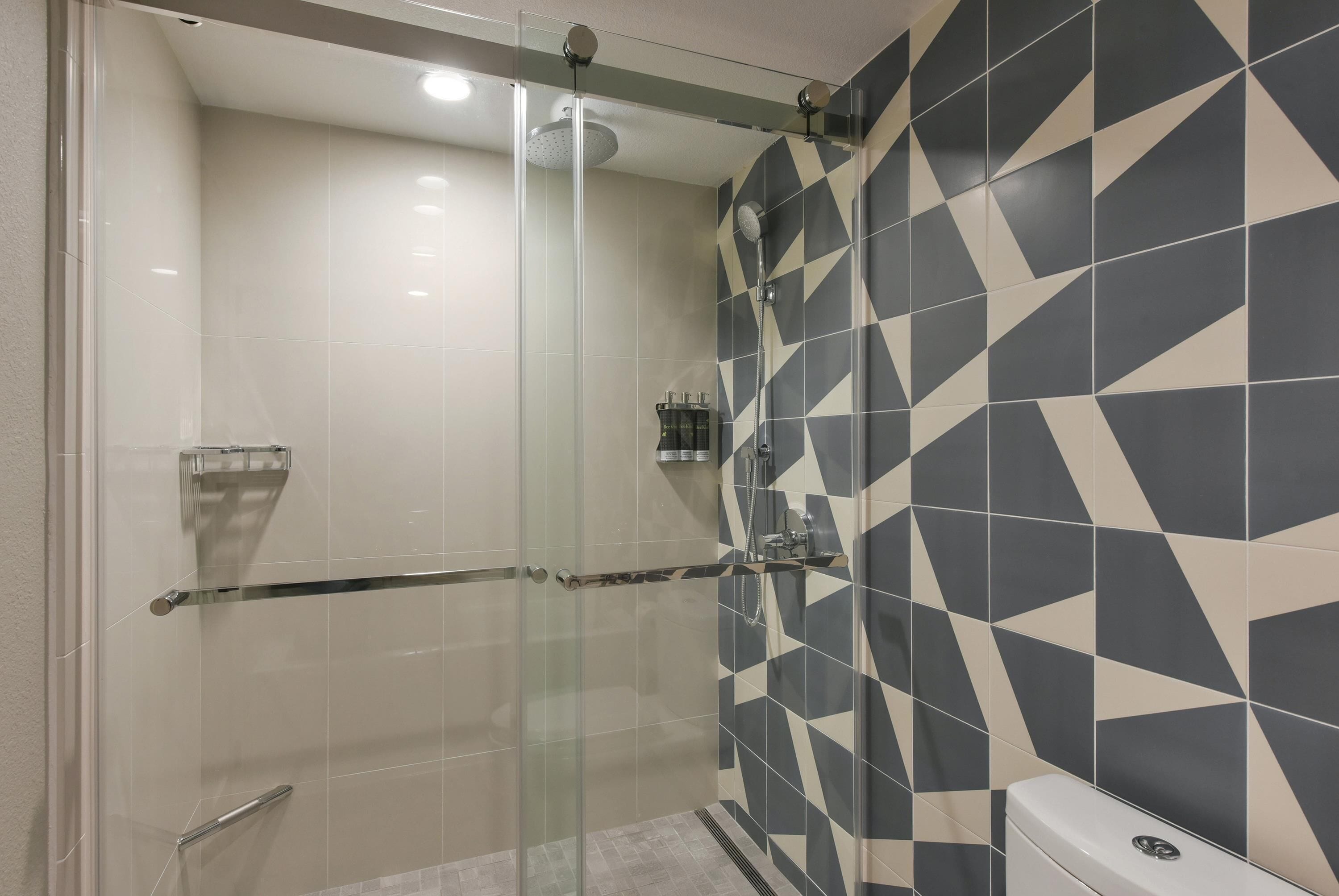 A modern bathroom with a glass-enclosed shower, geometric patterned tiles, and a toilet.
