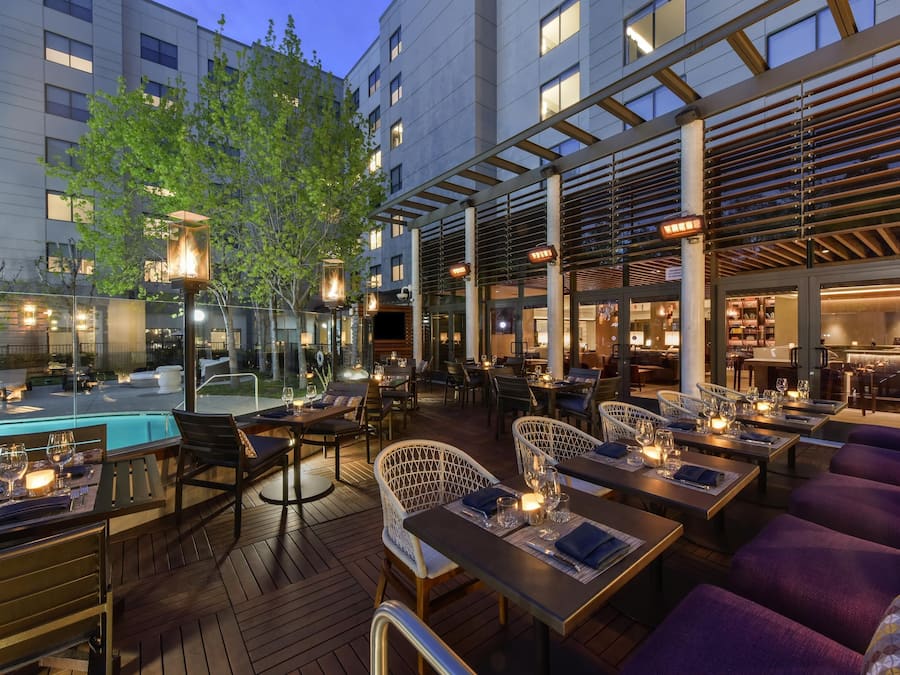 An outdoor dining area with tables and chairs, a pool, and a building in the background.