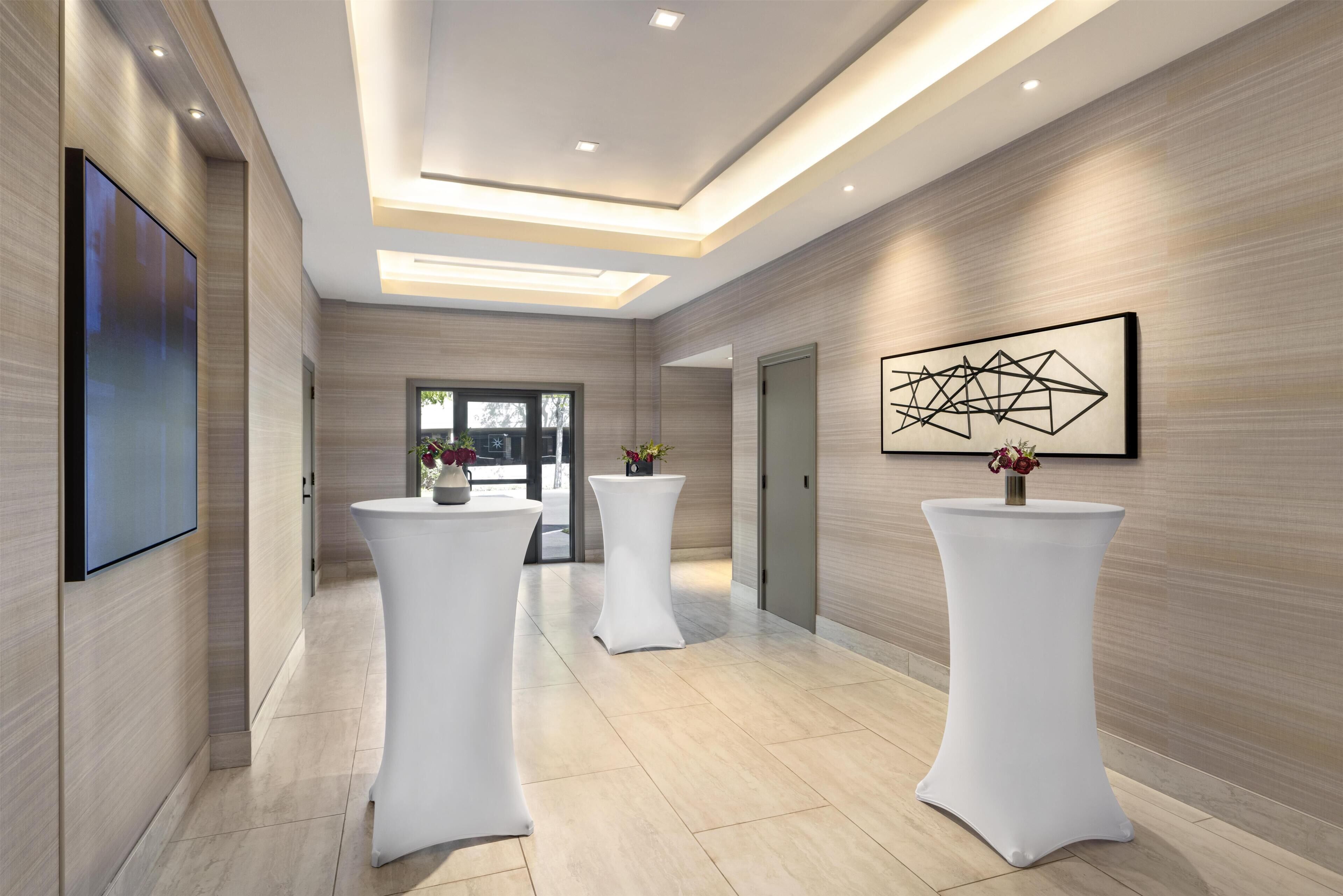 A modern hotel lobby with a high ceiling, recessed lighting, and a large abstract artwork on the wall.