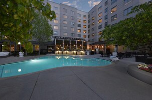 Un patio de hotel con piscina, mobiliario exterior y una zona de bar cubierta.