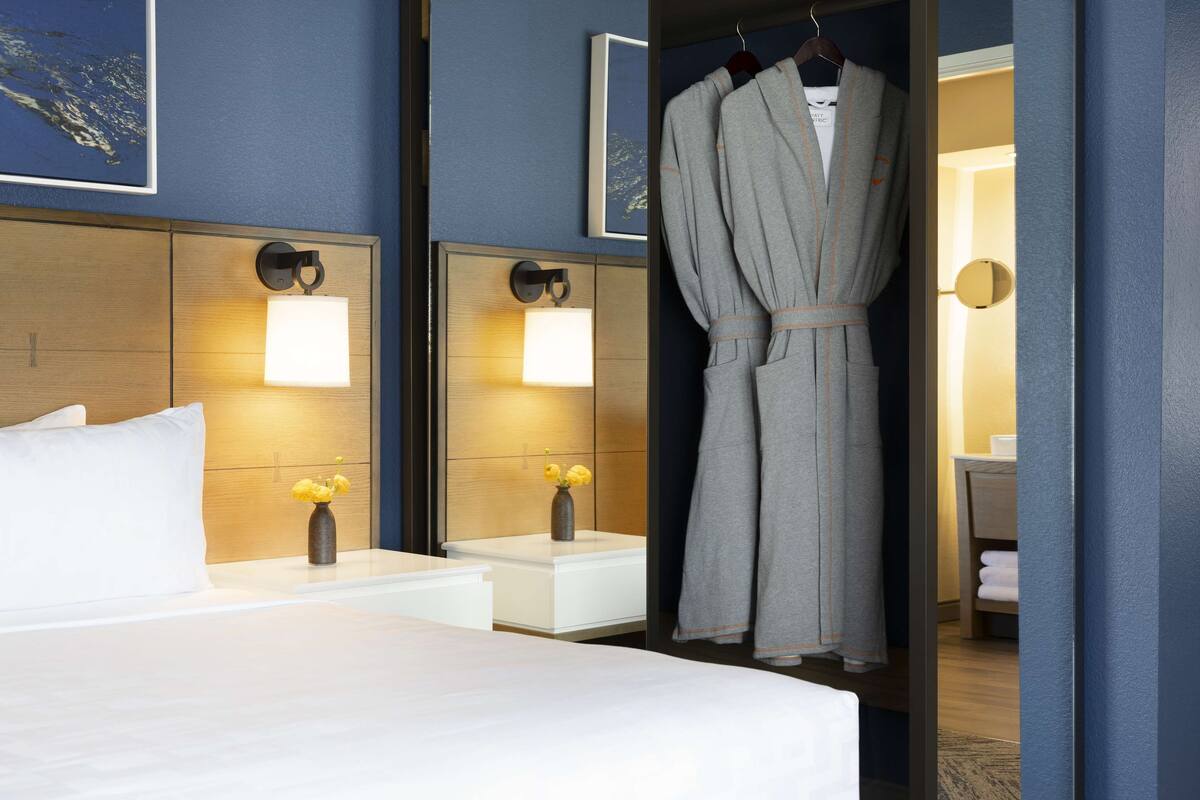 Une chambre d’hôtel avec un lit, des tables de chevet, une robe suspendue et un miroir.