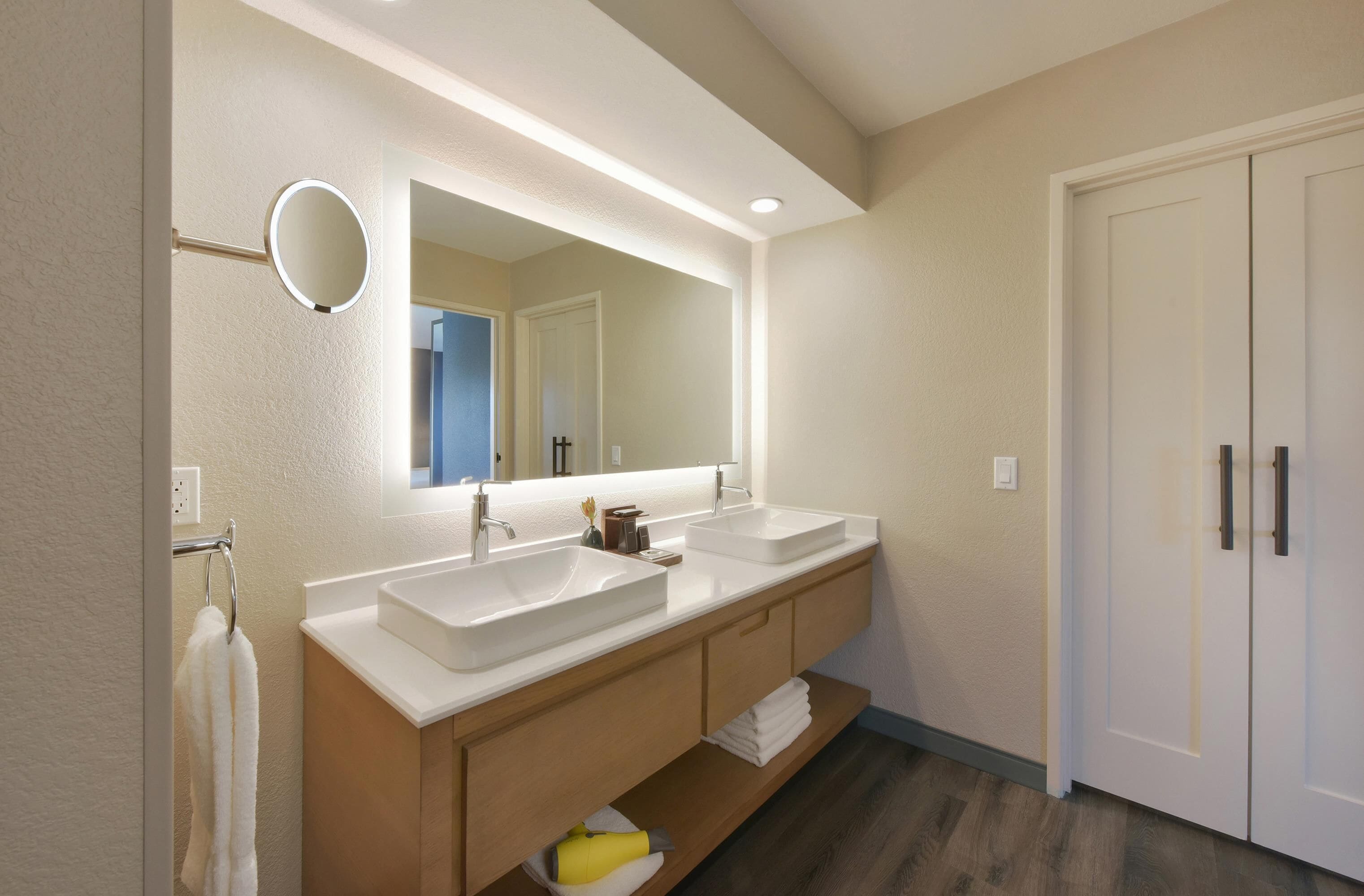 A modern bathroom with two sinks, a large mirror, and a door.