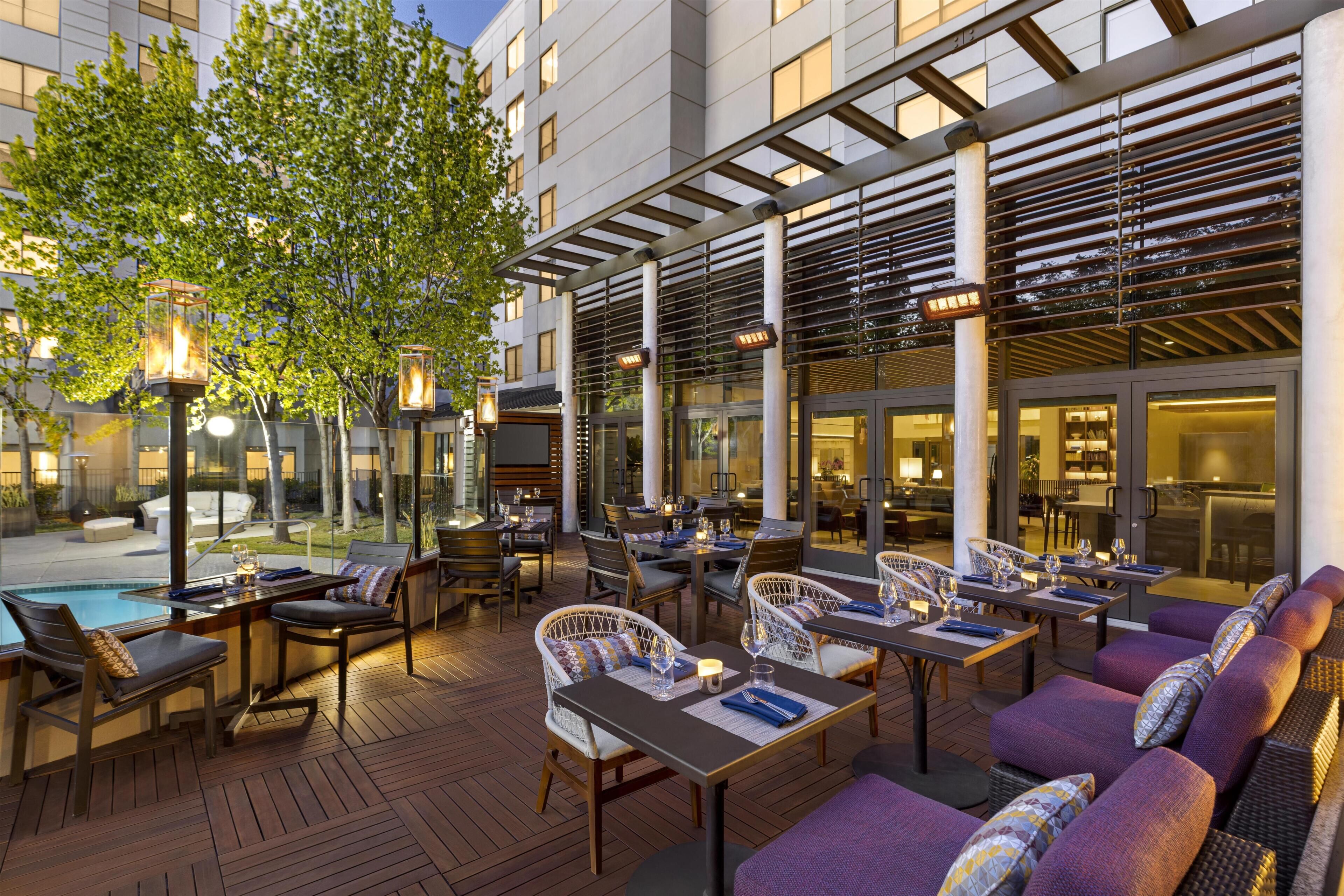 An outdoor dining area with tables and chairs, a pool, and a covered seating area with a pergola.