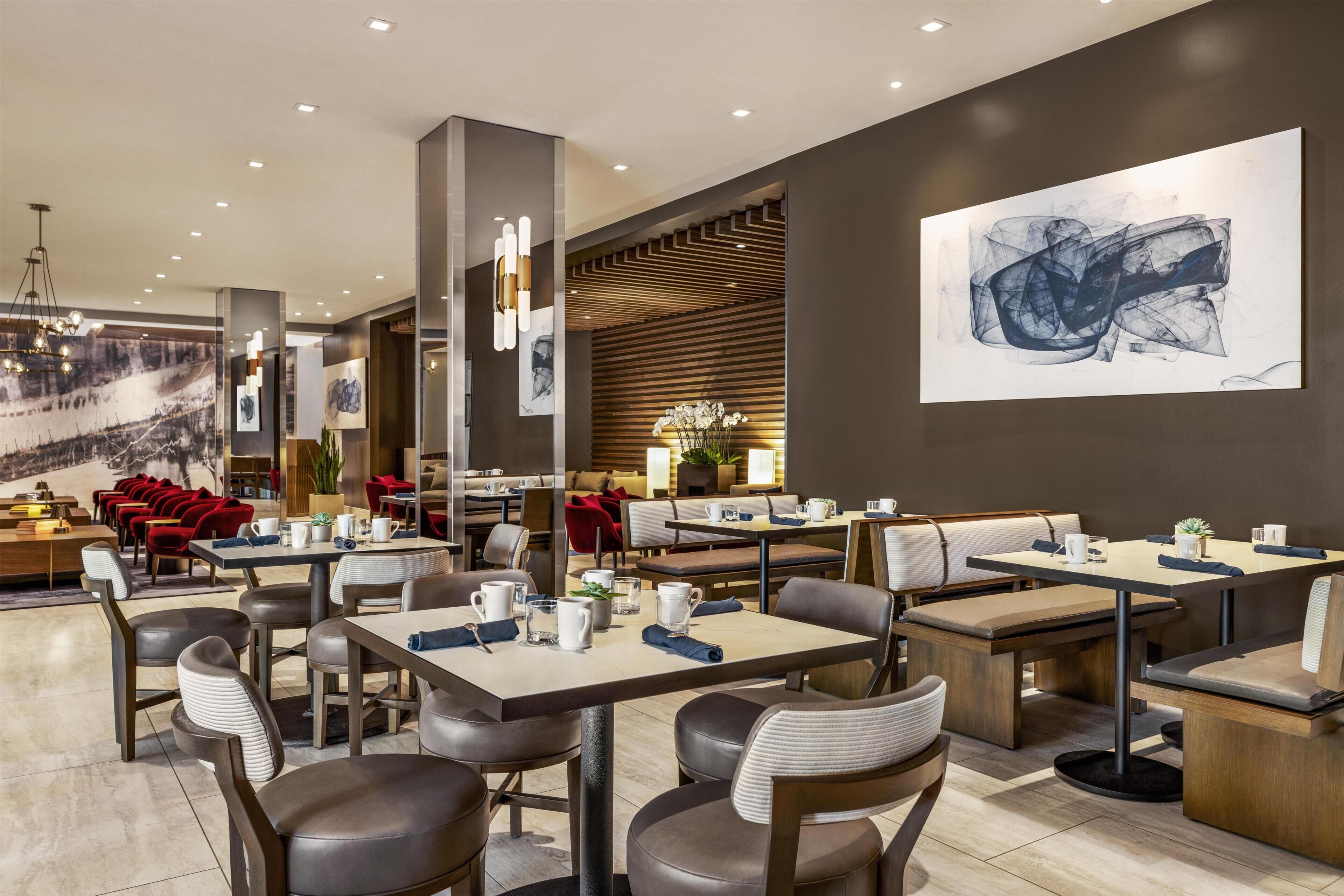 Un restaurante moderno con varias áreas de comedor, incluidas mesas y cabinas, y un cuadro abstracto de gran tamaño en la pared.