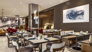 Un restaurante moderno con varias áreas de comedor, incluidas mesas y cabinas, y un cuadro abstracto de gran tamaño en la pared.