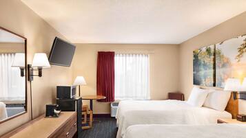 A hotel room with two beds, a flat-screen TV, a desk with a lamp, a mirror, and a painting on the wall.
