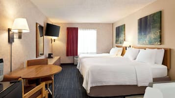 A hotel room with a bed, a desk, a chair, a TV, and artwork on the walls.