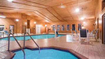 Une piscine intérieure aux murs et au plafond en bois, entourée de chaises longues et dotée d’un sol carrelé.