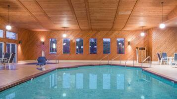 An indoor swimming pool with wooden walls and ceiling, multiple windows, and lounge chairs.