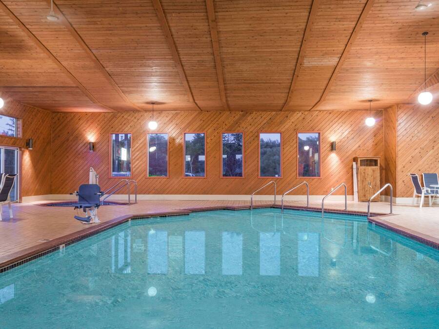 An indoor swimming pool with wooden walls and ceiling, multiple windows, and lounge chairs.