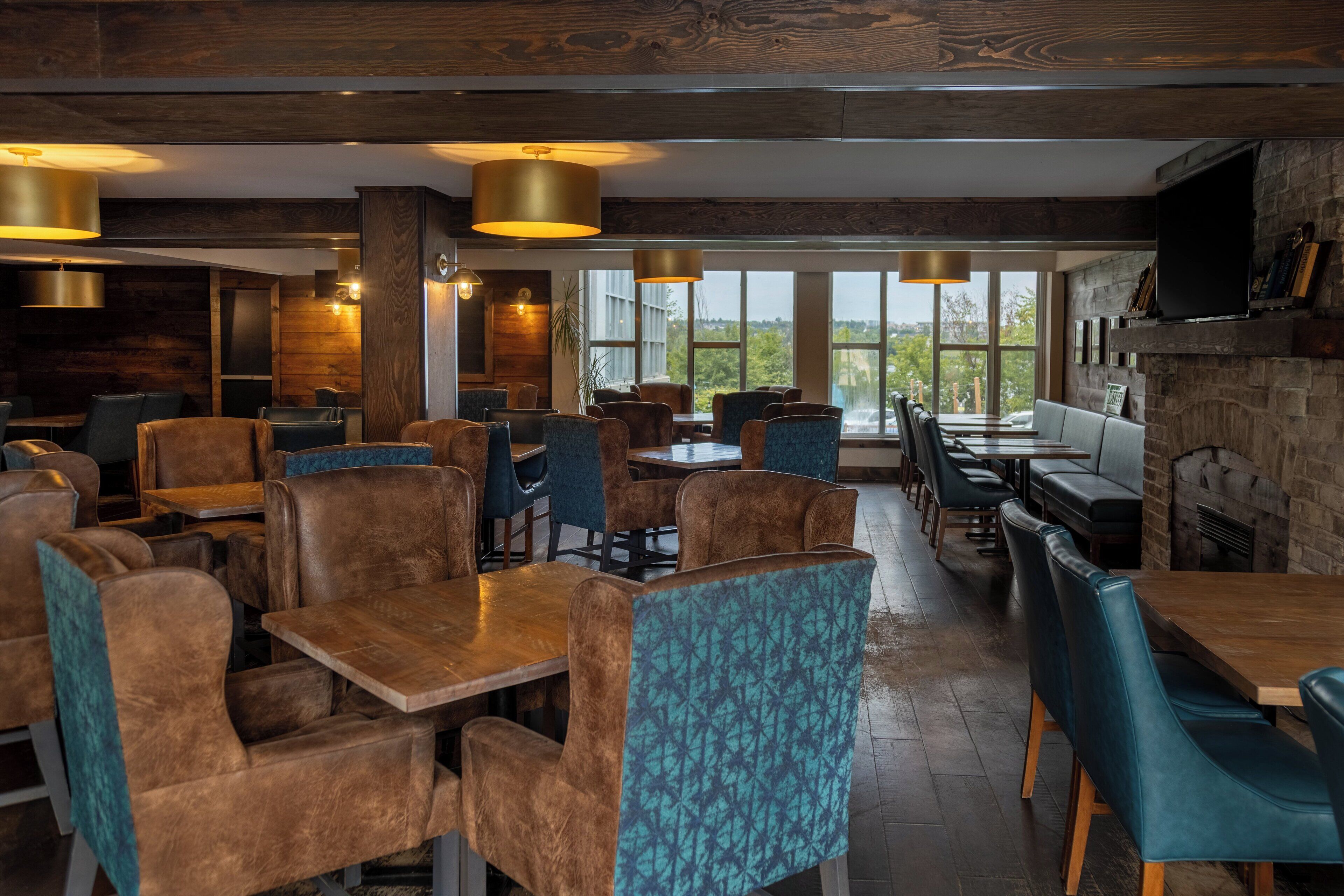 Un restaurant avec des tables et des chaises en bois, de grandes fenêtres et une cheminée en pierre.