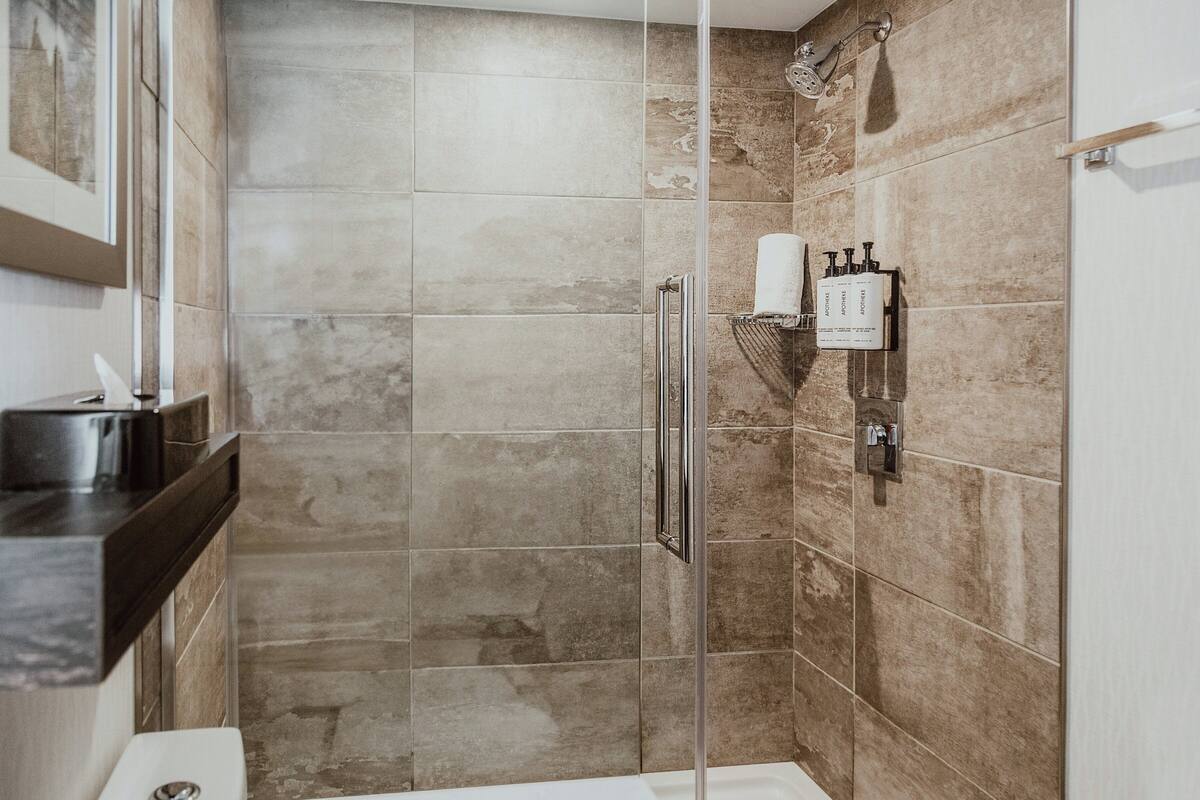 Une salle de bain moderne dotée d’une douche à parois de verre, de toilettes et d’un lavabo avec un plan de travail noir.