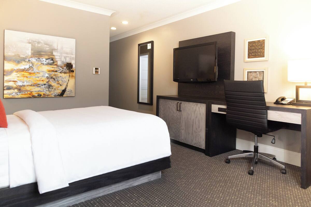 Une chambre d’hôtel équipée d’un lit, d’un bureau, d’une chaise, d’une télévision et d’œuvres d’art accrochées au mur.
