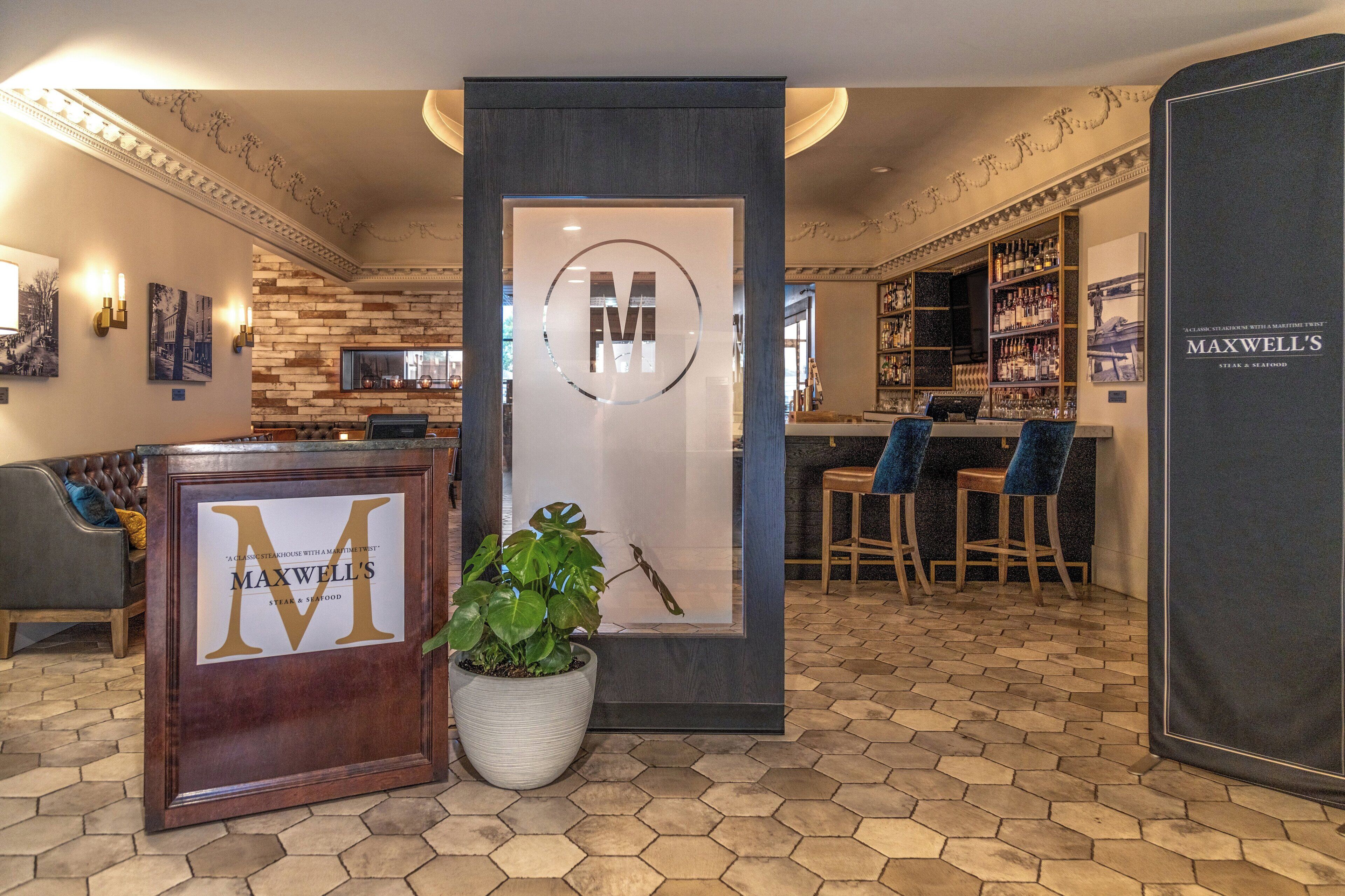 A bar area with a large 'M' logo, a potted plant, and hexagonal patterned flooring.