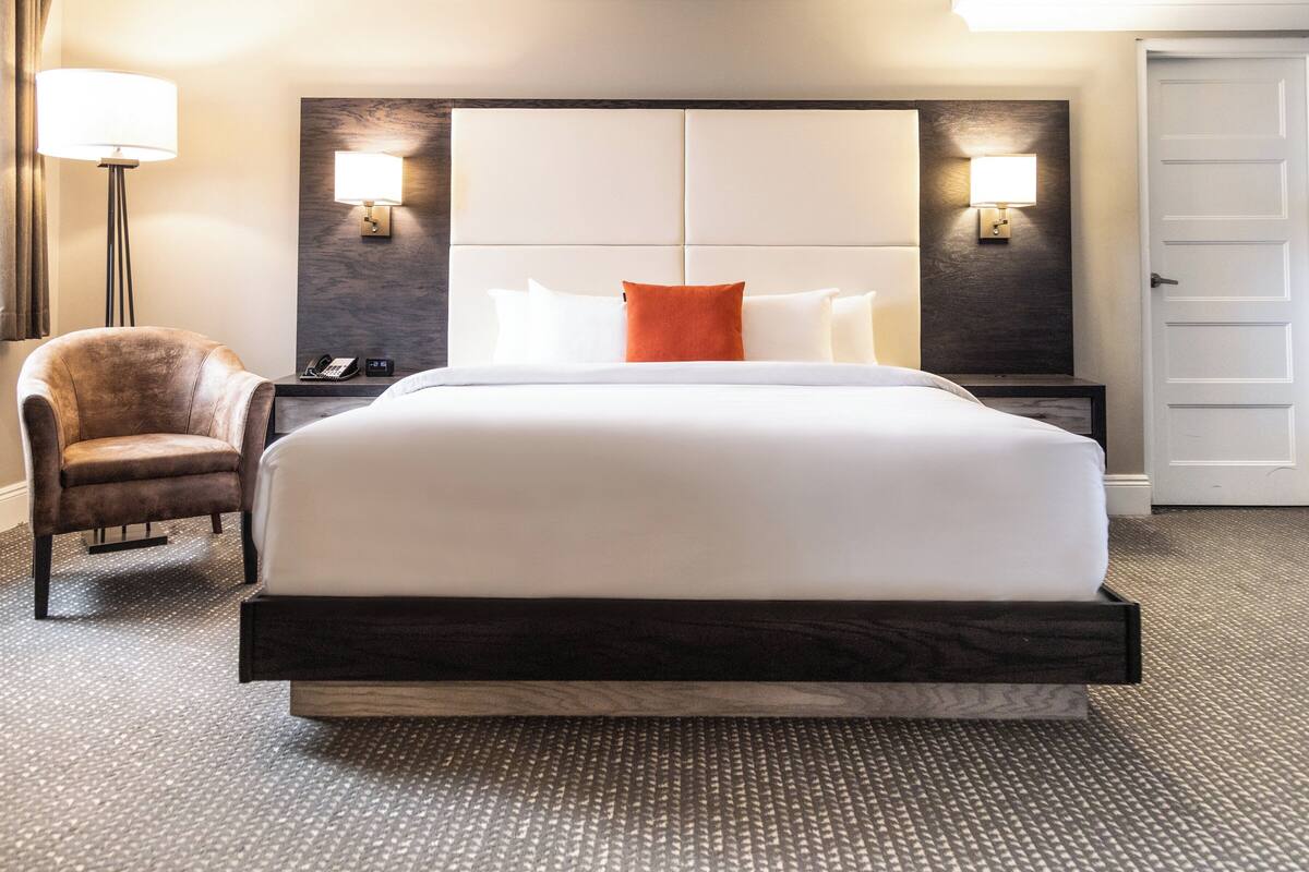 A hotel room with a large bed, two bedside tables, a chair, and a door.