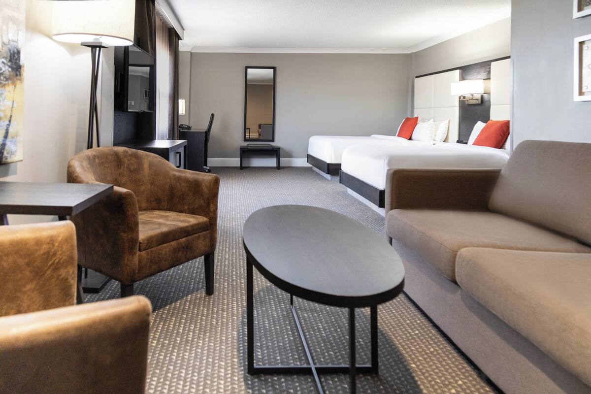 Une chambre d’hôtel comprenant un lit, deux fauteuils, une petite table, un bureau et un miroir.