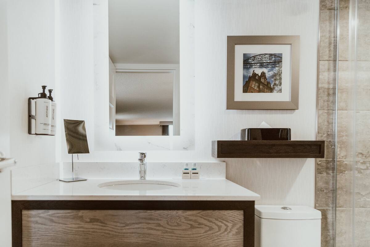 Une salle de bain moderne avec un lavabo blanc, un miroir, un tableau encadré au mur et un meuble-lavabo en bois.
