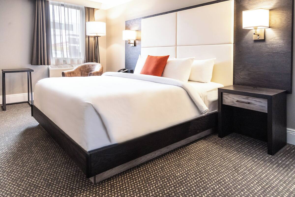 A hotel room with a large bed, a bedside table, a chair, and a lamp.