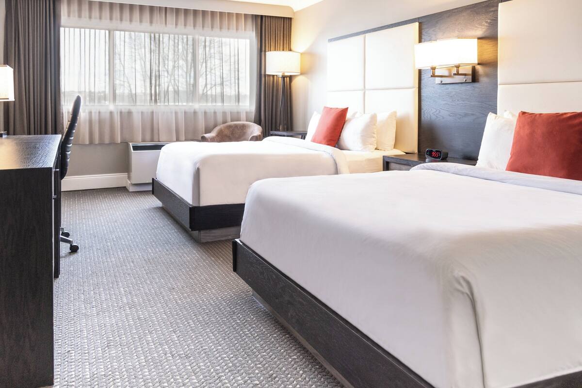 A hotel room with two beds, a desk, a chair, and a window with curtains.