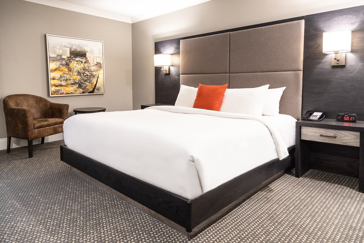 Een hotelkamer met een groot bed, een bruine fauteuil, een kleine tafel, een wandlamp en een schilderij aan de muur.