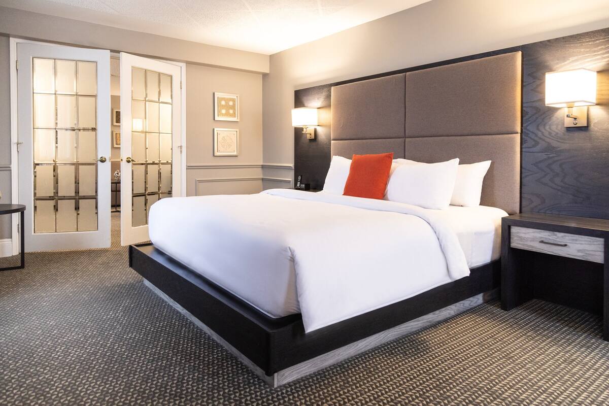 A hotel room with a large bed, a nightstand, a wall-mounted lamp, and a door with frosted glass panels.