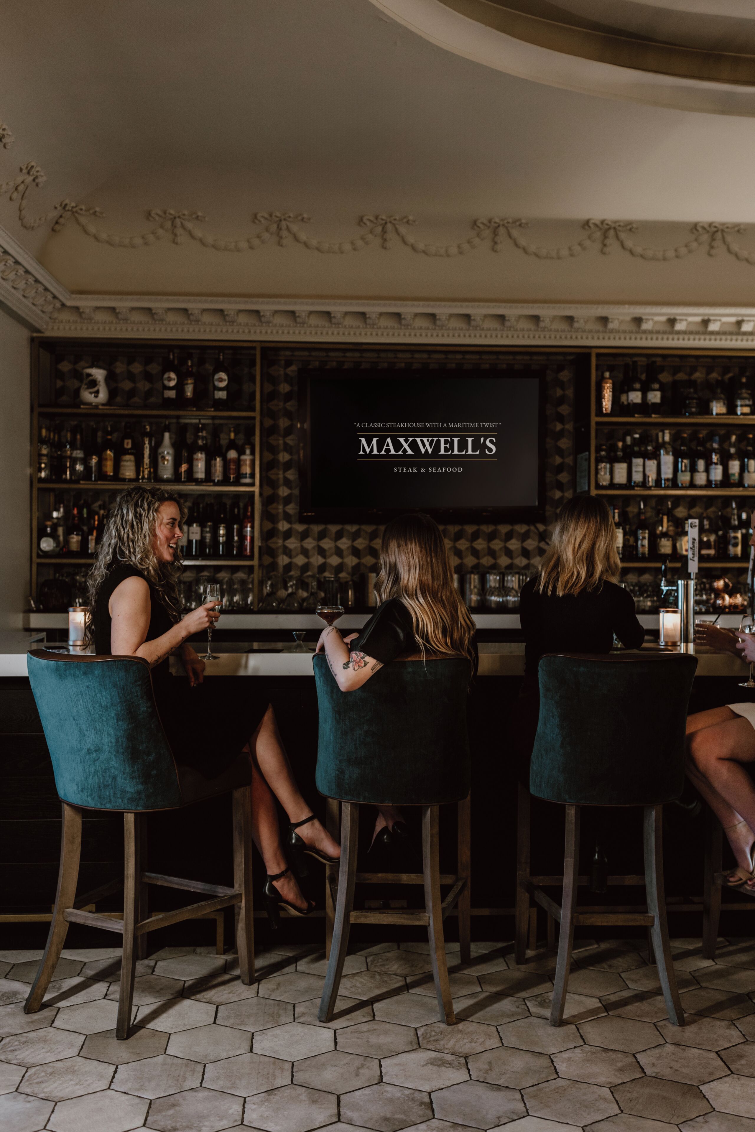 Zona de bar con tres taburetes, un menú colgado en la pared y una estantería con botellas.