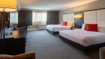 Una habitación de hotel con dos camas, un escritorio, una silla, un televisor y un ventanal grande con cortinas.