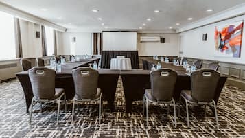 Une salle de conférence avec une longue table, des chaises, des bouteilles d’eau et un écran de projection.