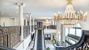 Uma escadaria imponente com grades ricamente decoradas, um candelabro e uma varanda com vista.