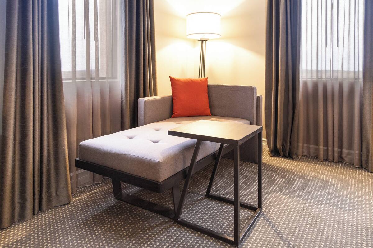 A hotel room with a sofa bed, a small table, and a lamp.