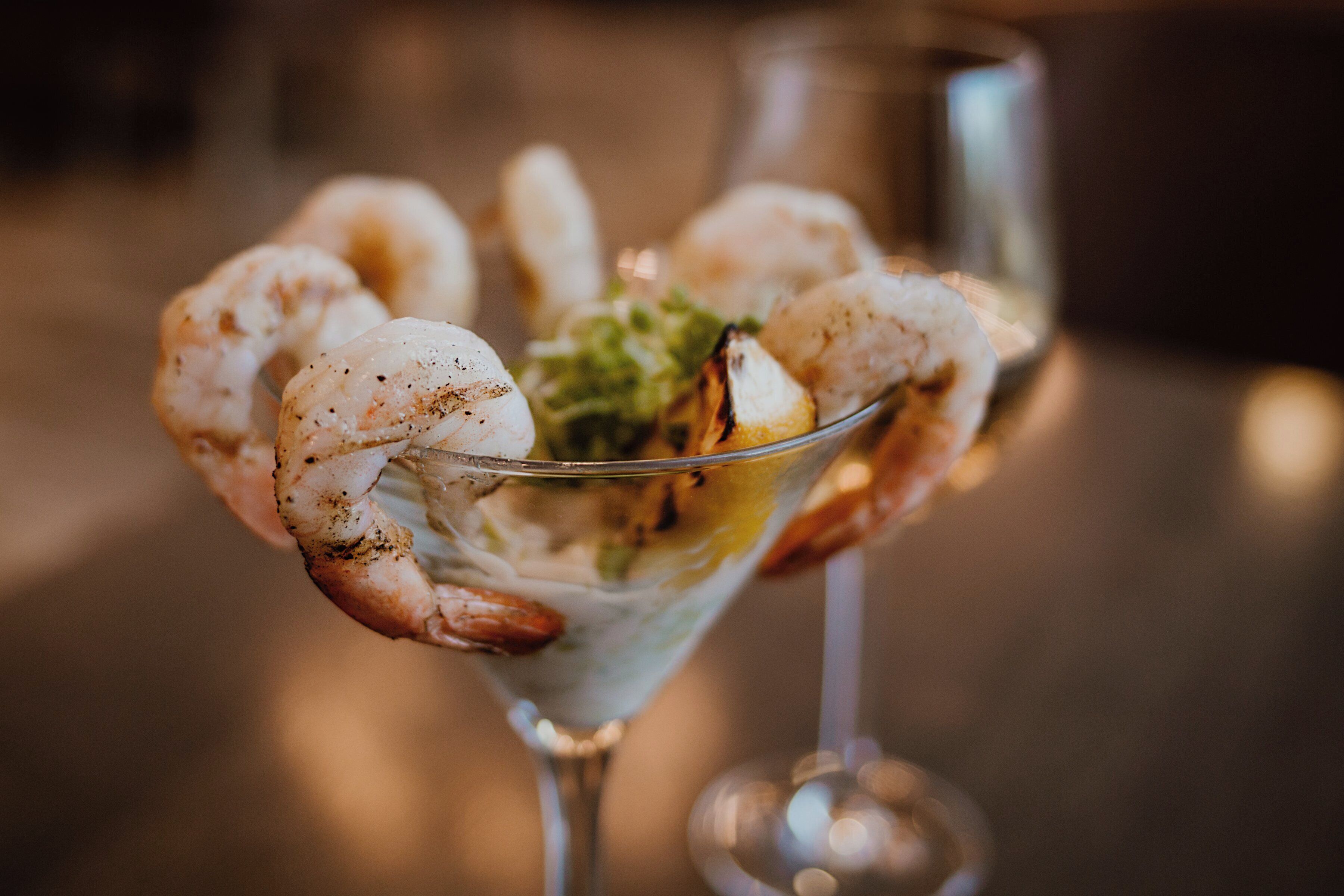 A martini glass with grilled shrimp and a garnish.