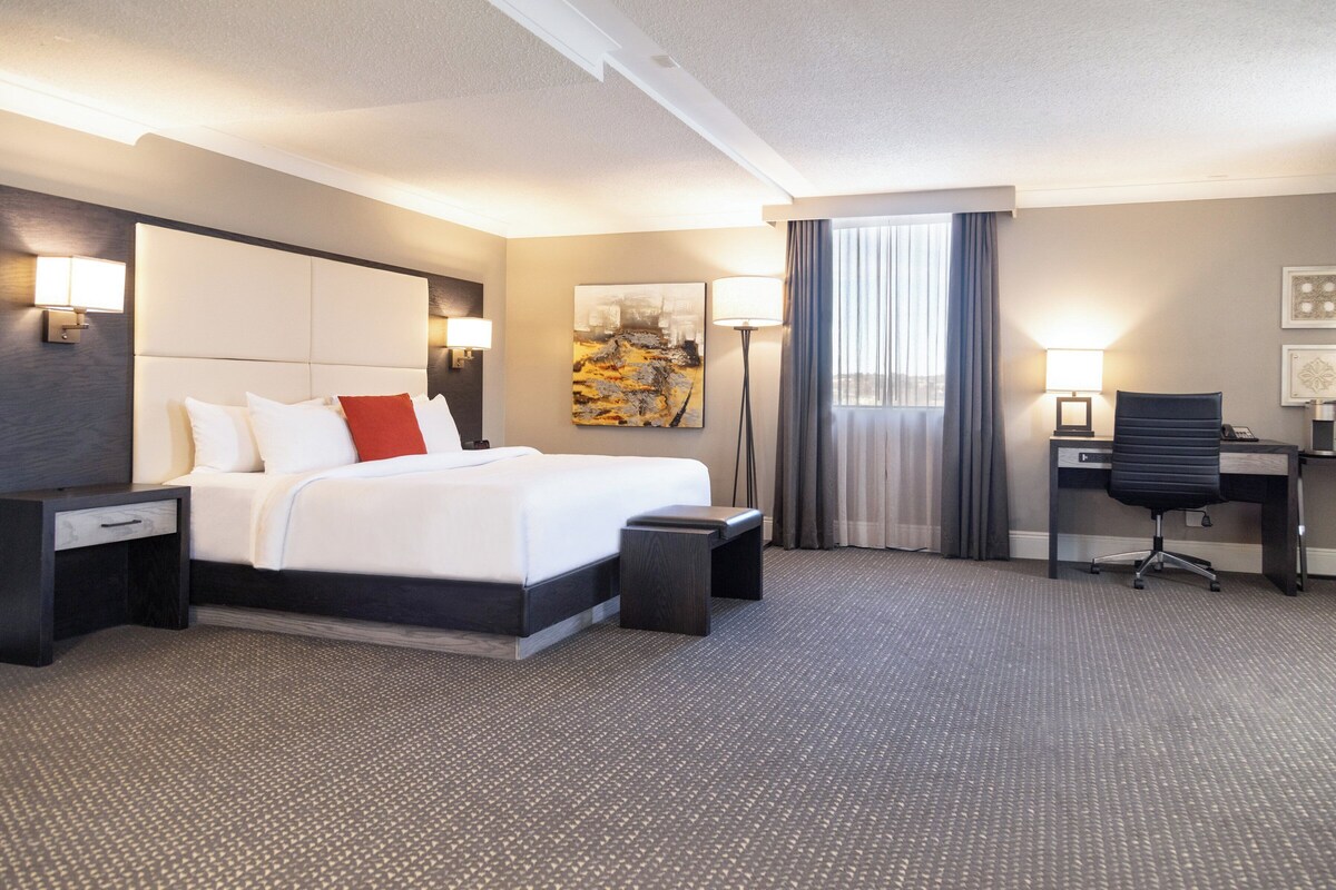 Een hotelkamer met een groot bed, een bureau, een stoel en een raam met gordijnen.