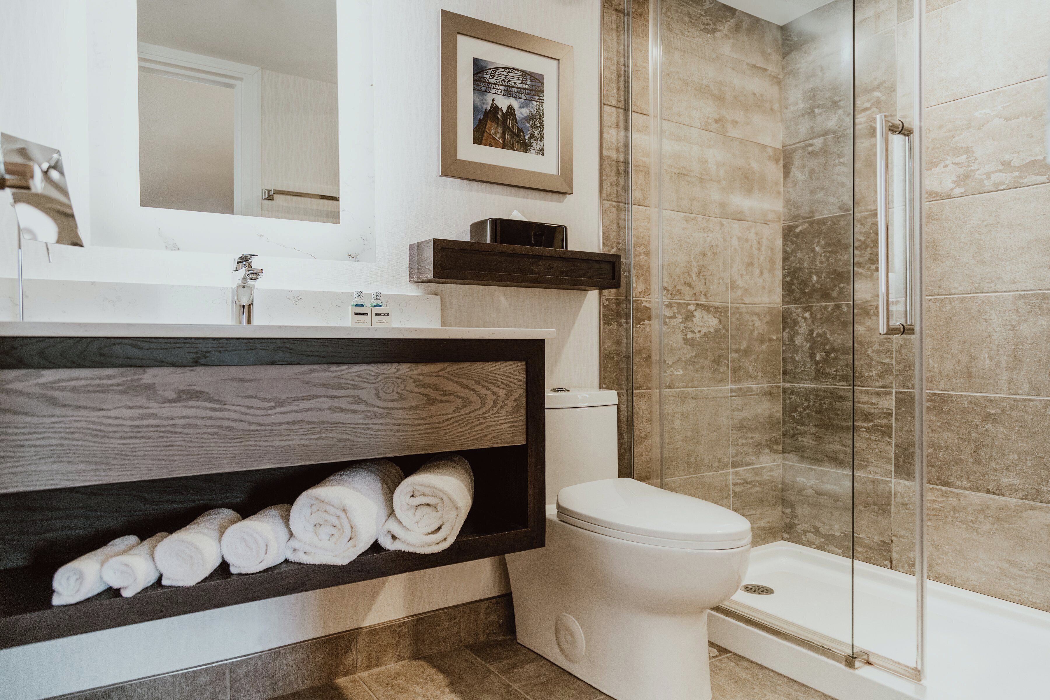 Un baño moderno con ducha, inodoro y un estante con toallas enrolladas.
