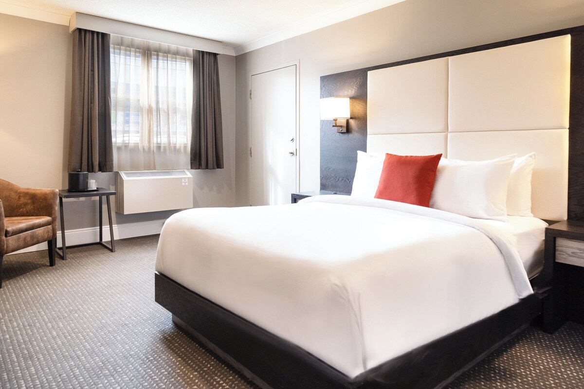 Een hotelkamer met een groot bed, een bureau, een stoel en een raam met gordijnen.