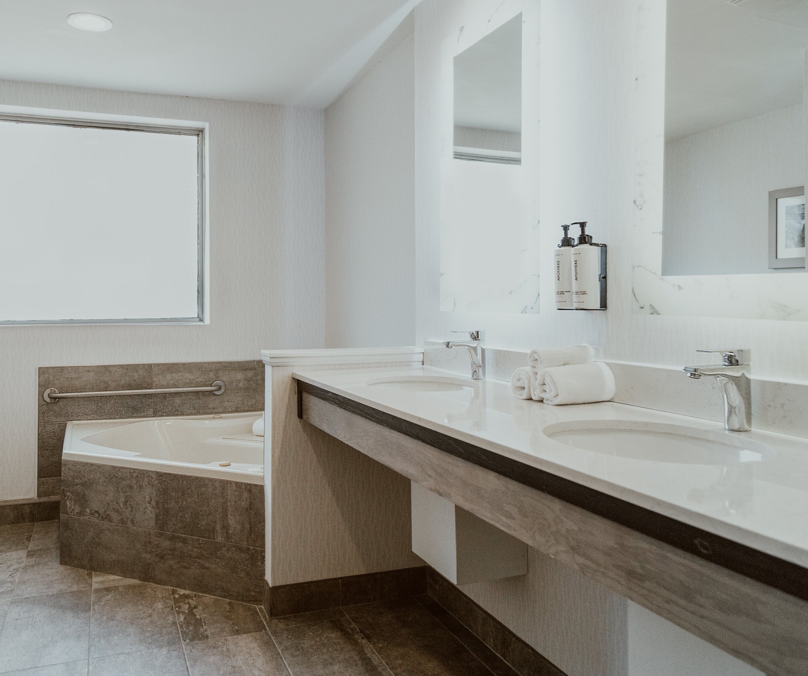 A modern bathroom with two sinks, a large mirror, and a bathtub.