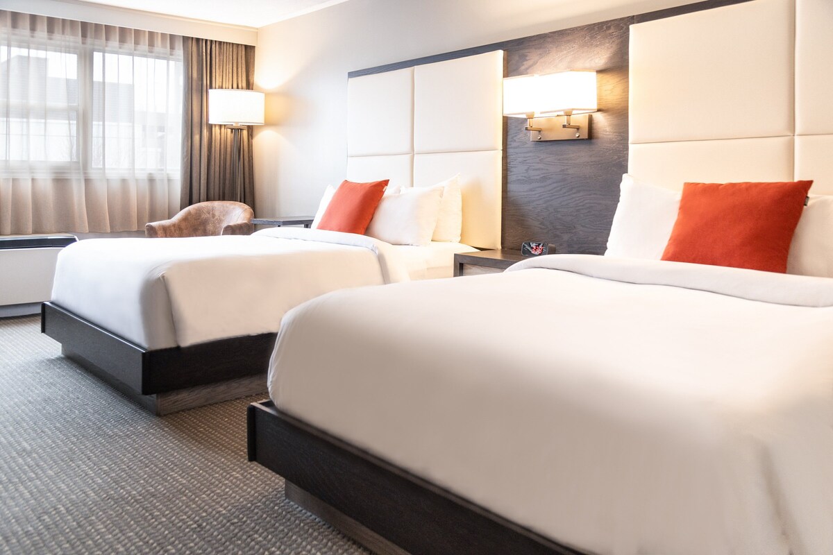 Een hotelkamer met twee bedden, een stoel, een nachtkastje en een lamp.