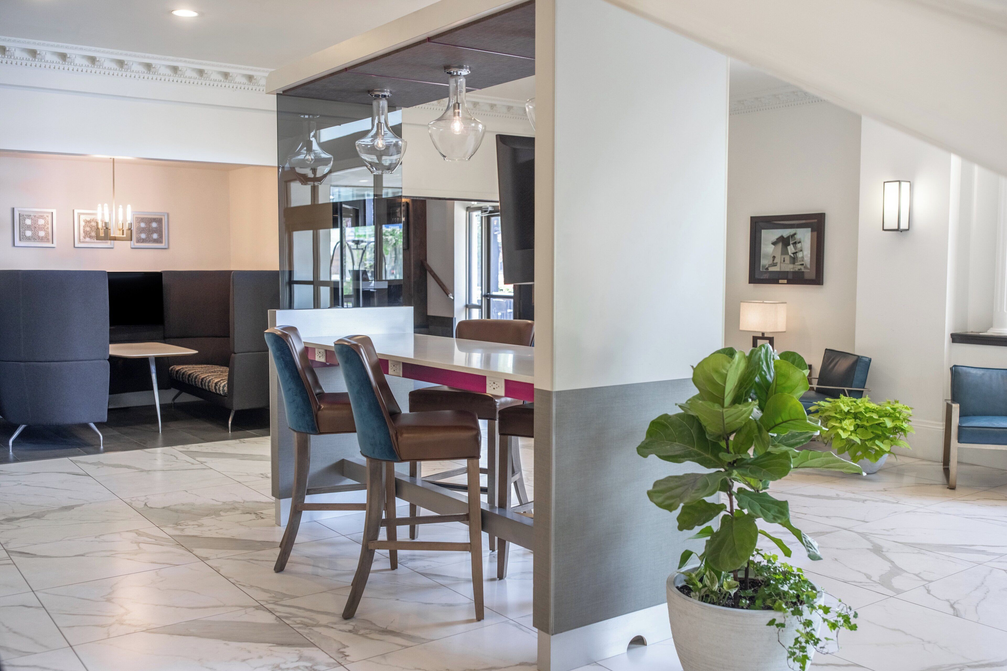 Un moderno vestíbulo de hotel con piso de mármol, un área de comedor con sillas y mesa de madera, y una planta grande en maceta.
