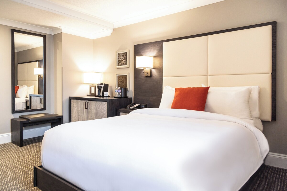 Een hotelkamer met een groot bed, nachtkastje, kaptafel, spiegel en een wandlamp.