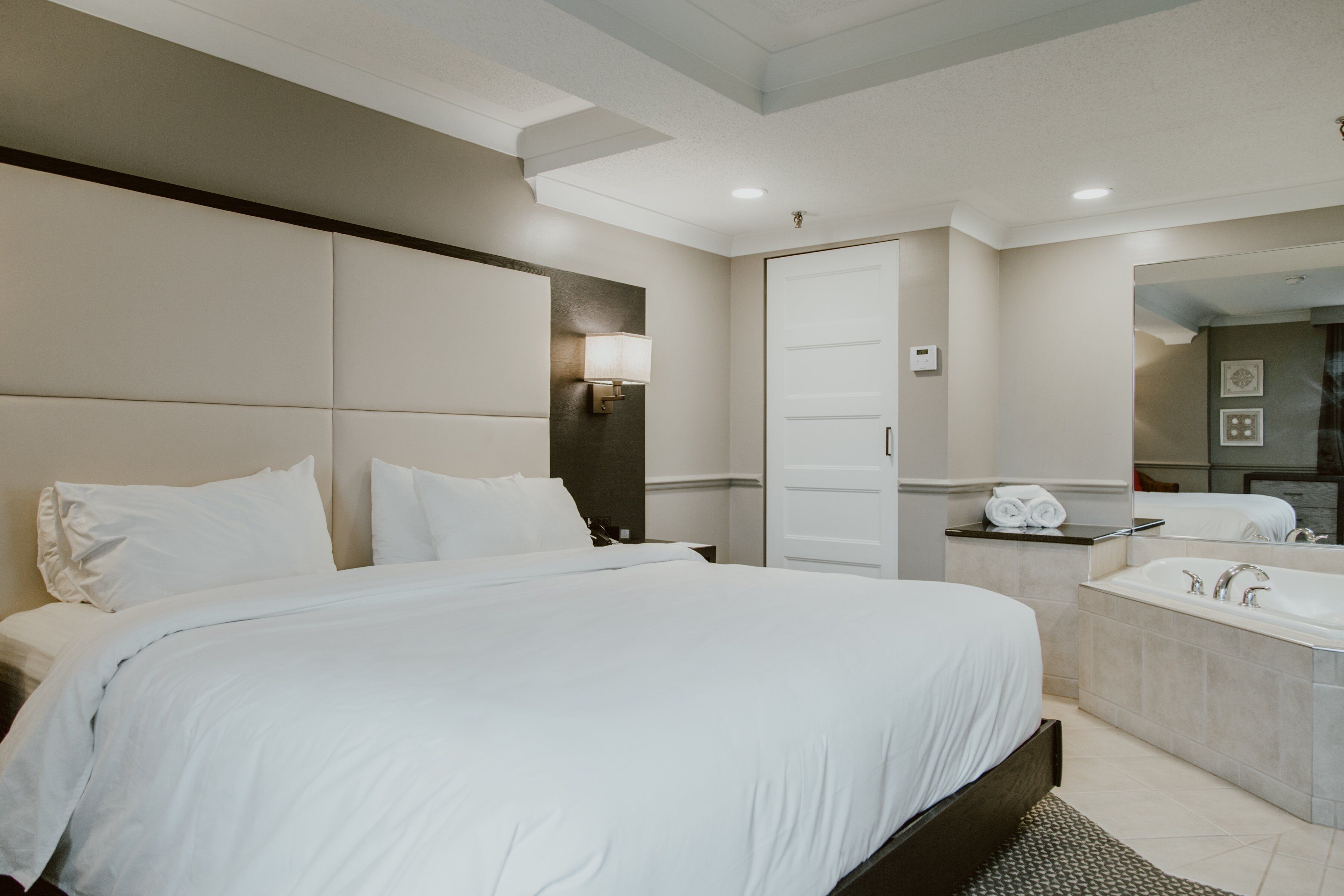 A modern hotel room with a large bed, a bathroom with a bathtub, and a mirror.