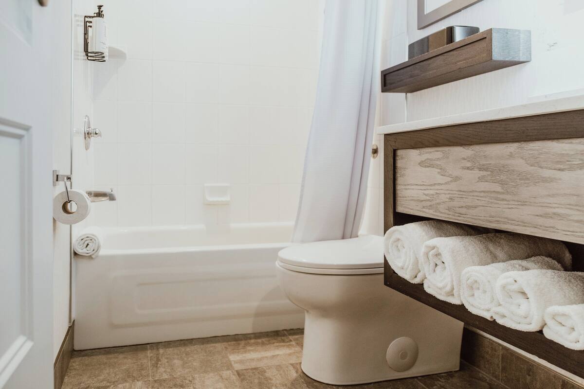 Une salle de bain avec une baignoire blanche, des toilettes et une étagère où sont pliés des serviettes.