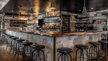 A bar area with a stone counter, multiple stools, and shelves stocked with bottles and glasses.