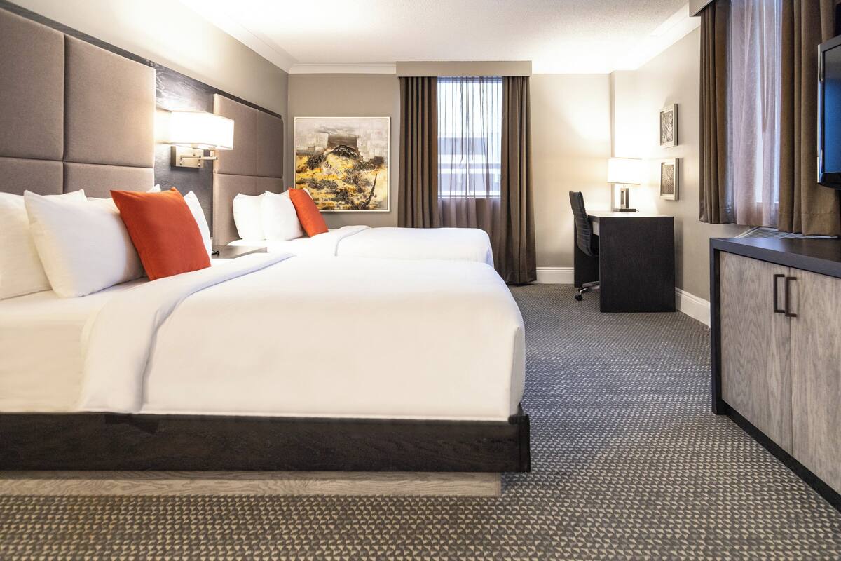 A hotel room with a large bed, a desk, a television, and a painting on the wall.